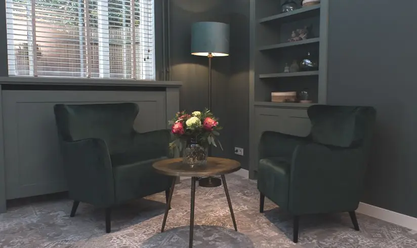 Hoek van een kamer 2 grote groene fauteuils en een salontafeltje